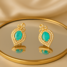Gold earrings with turquoise stones on a reflective surface