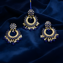 Set of gold and blue earrings on a dark blue fabric background