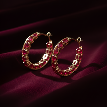 Gold hoop earrings with red gemstones on a dark purple fabric background