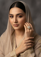 Woman wearing a beige embroidered outfit with a ring on her finger against a dark background