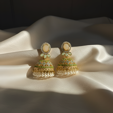 Ornate earrings with green and gold details on a white fabric background