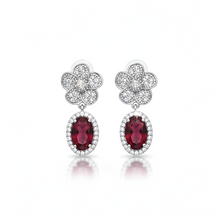 Pair of earrings with red gemstones and silver floral designs on a white background