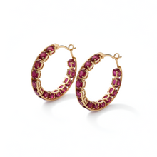 Pair of gold hoop earrings with red gemstones on a white background