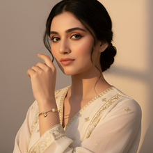 Woman in a white traditional outfit with gold accents, posing against a warm-toned wall.