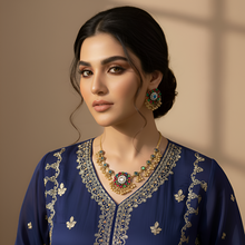 Woman wearing a blue embroidered outfit with gold jewelry against a beige background