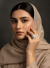 Woman wearing a beige hijab and embroidered outfit, holding a diamond ring.