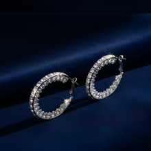 Silver hoop earrings with clear stones on a dark blue fabric background