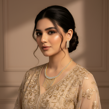 Woman wearing a gold embroidered outfit with jewelry against a neutral background