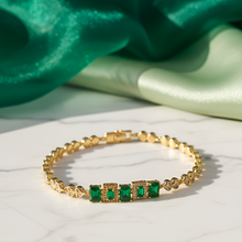Gold bracelet with green gemstones on a white surface with green fabric in the background