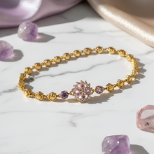 Gold bracelet with pink gemstone on a marble surface with amethyst crystals